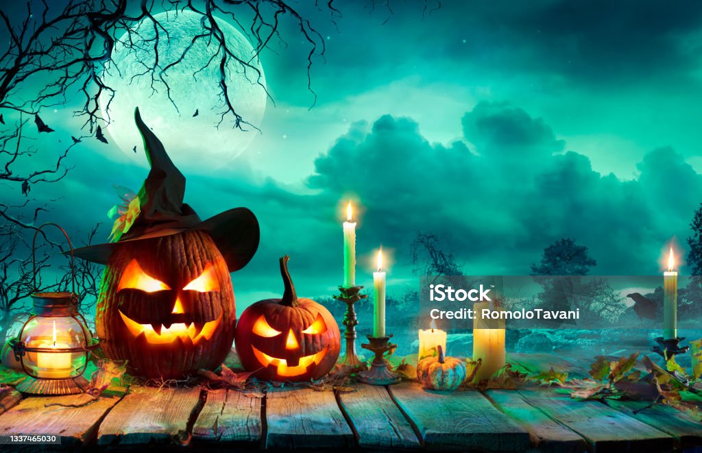 Halloween At Night - Pumpkins With Witch Hat And Candles On Table In Mystery Landscape Jack o' Lantern On Wooden Table With Leaves And candlestick Candle Stock Photo