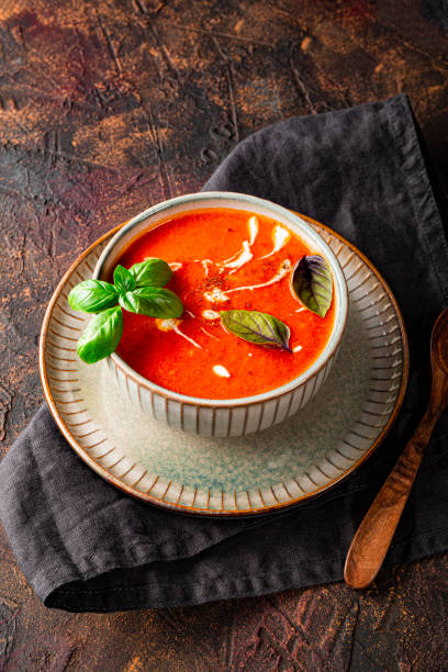 un plato de sopa de tomate tradicional de españa con crema y albahaca en la mesa foto vertical. gazpacho de tomate y albahaca en un cuenco gris - sopa de tomate fotografías e imágenes de stock