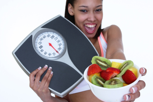 woman holding weight scale and a bowl of fruit