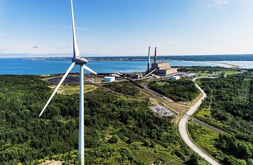 Aerial drone view of a wind turbine in the foreground of a coal fired power generating station.