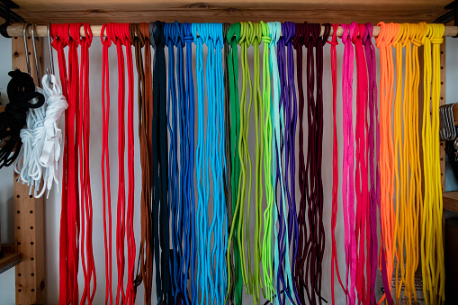 A front view close up view of a colourful workspace with organised shoelaces that have been tied neatly on a rack and are organised into a rainbow type of pattern. / Female Focus Collection
