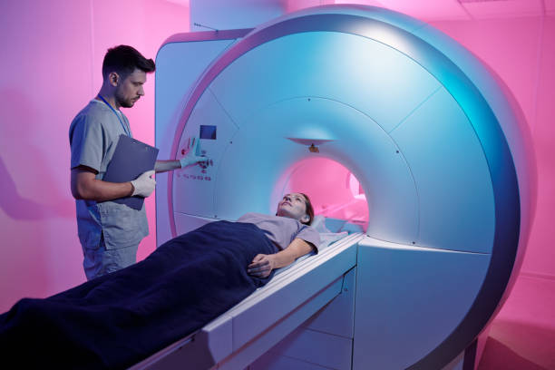 istock Young doctor in uniform pressing start button of mri scan machine with patient 1337470107