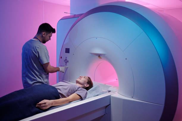 Young doctor pushing button on panel to start mri scan procedure Young doctor pushing button on panel to start mri scan procedure while female patient lying on long table mri scanner stock pictures, royalty-free photos & images