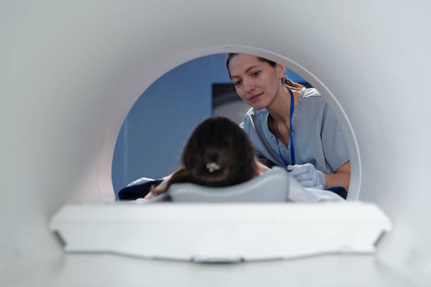 joven clínica mirando a la niña acostada en la mesa de la resonancia magnética - mri scanner fotografías e imágenes de stock