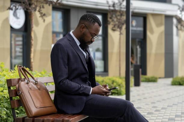 istock Young businessman of African ethnicity texting in smartphone while resting on bench 1337472680