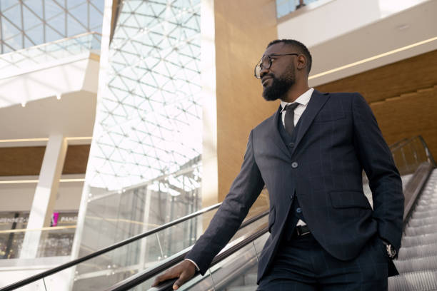 istock Young confident businessman in suit standing on escalator while moving downwards 1337472746