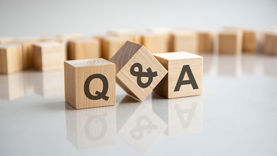 Q and A - an abbreviation of wooden blocks with letters on a gray background. Reflection of the Q and A caption on the mirrored surface of the table. Selective focus.