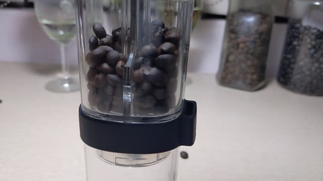 Slow motion. Roasted coffee beans are poured into a manual retro coffee grinder to grind it into powder. Top view, closeup.