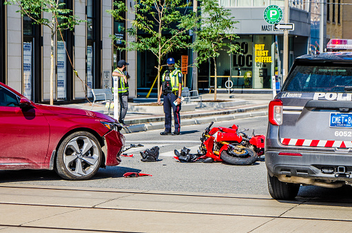Motorcycle hit by car on Toronto street during summer day.
Police car on the site too.
