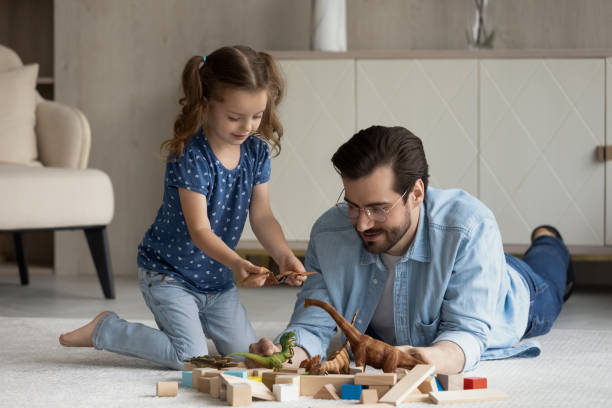 istock Dad and little daughter engaged in game, playing with dinosaurs 1337484906