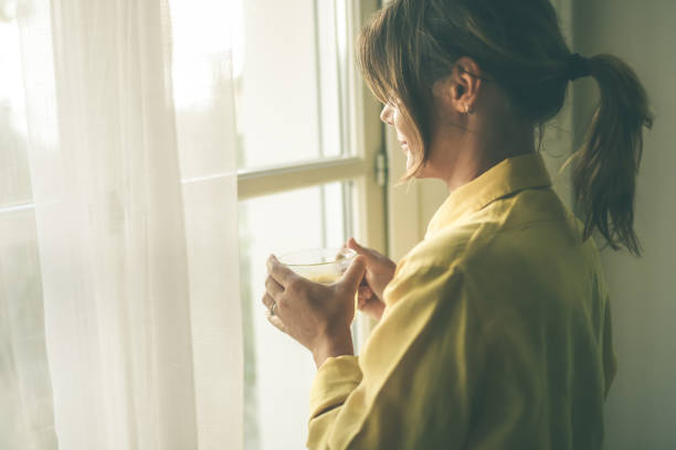 istock Woman drinking a cup of tea looking outside the window 1337487510