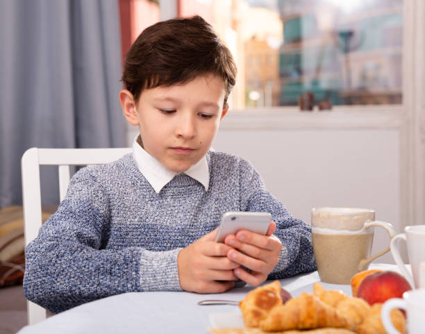 istock Boy looking to smartphone screen at the table in the kitchen 1337488383