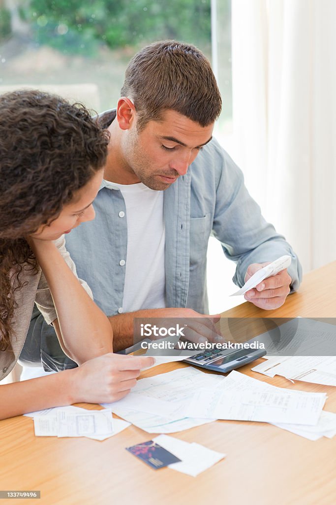 Young couple using calculator to do their bills at the table Young couple calculating their domestic bills at home Adult Stock Photo