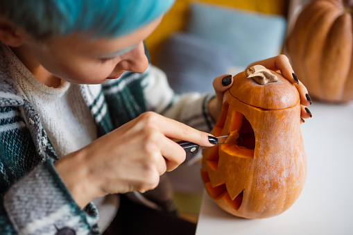 Young cheerful Caucasian woman carving pumpkin for Halloween at home.