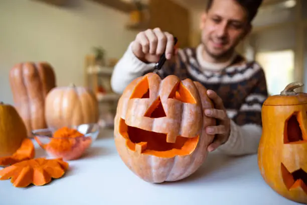 Photo of Handsome man carving a pumpkin for Halloween at home