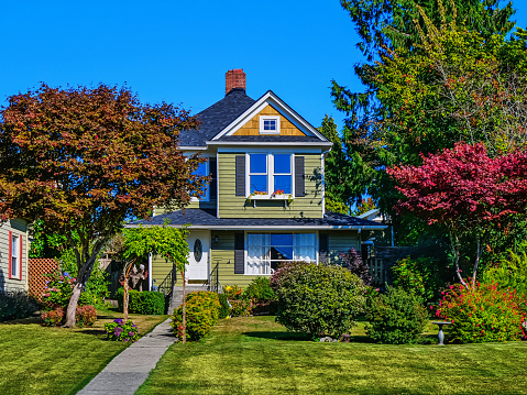 Photo of a small, green American suburban home exterior on a sunny summer day with clear blue sky, surrounded by colorful trees