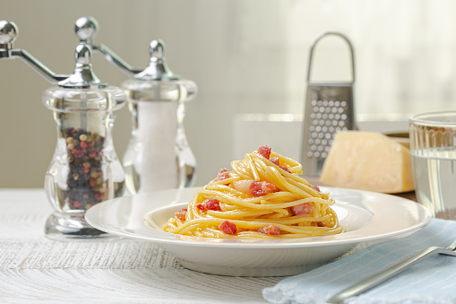 Lunch with pasta carbonara on a white wooden table. Spaghetti, pancetta and sauce made of egg yolk and parmesan cheese, traditional recipe.