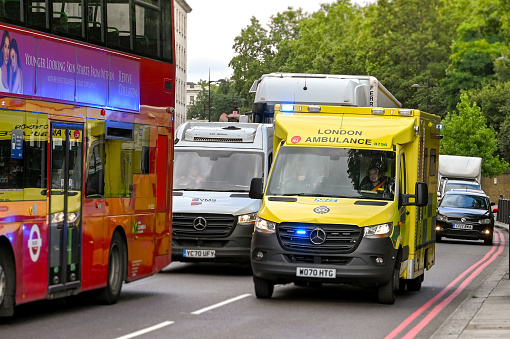 London, England - August 2021: London ambulance with blue lights flashing driving through traffic in central London in response to an emergency call.