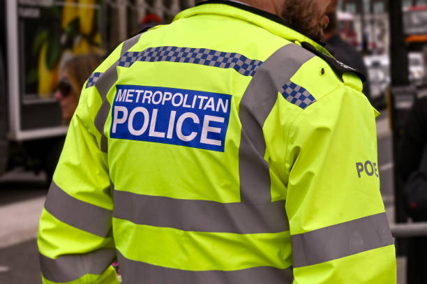 Rear view of a police offers from the Metropolitan Police London, England - August 2021: Rear view of a Metropolitan Police officer wearing a reflective jacket. In the background are crowds of people. metropolitan police stock pictures, royalty-free photos & images