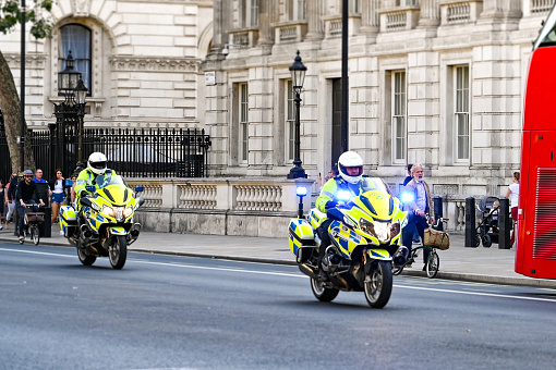 London, England - August 2021: Police officers on motorbikes with blue lights flashing driving down a street in central London