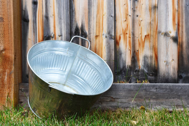 An image of an old galvanized washtub leaning against a wooden fence.