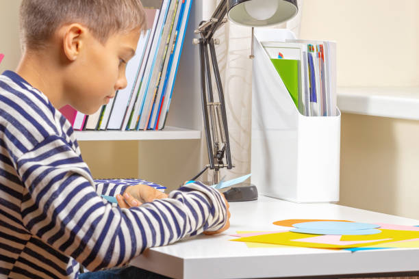 istock Education, learning, paper craft, entertainment. Boy cuts colored paper with scissors and making craft project at home 1337505228