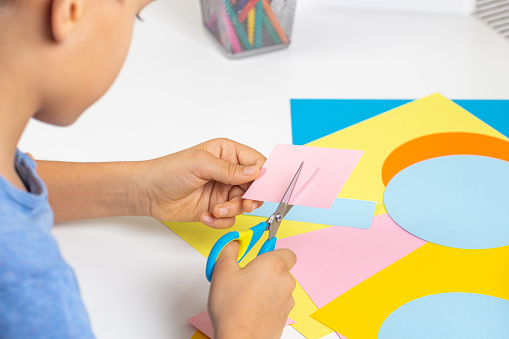 Kid hands cutting colored paper with scissors. Education, learning, paper craft, entertainment