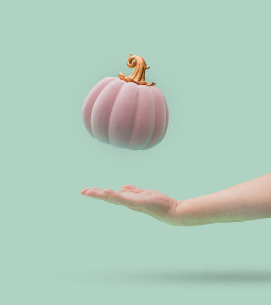 Pink Halloween pumpkin with golden petiole falling into women arm. Green mint background. Minimal design. Pink Halloween pumpkin with golden petiole falling into women arm. Green mint background. Minimal design. buggy eyes stock pictures, royalty-free photos & images