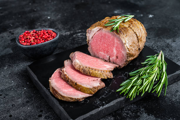 roastbeeffilet filetfleisch auf einem marmorbrett. schwarzer hintergrund. draufsicht - kalbfleisch stock-fotos und bilder