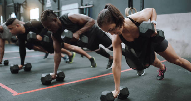 photo d’un groupe de jeunes sportifs faisant des pompes et des rangées de renégats ensemble dans un gymnase - human muscle muscular build dumbbell sports training photos et images de collection