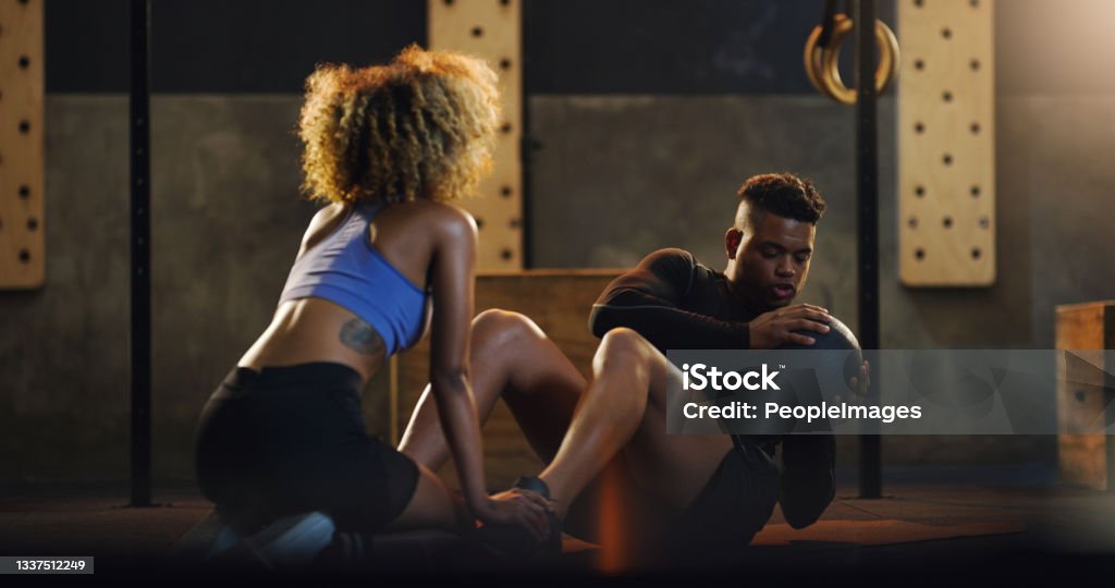 Shot of a young man doing russian twists with a weighted ball and the help of a trainer in a gym Building a stronger core with every twist Gym Stock Photo