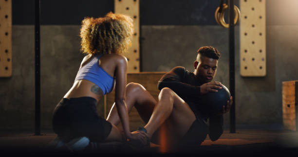 Shot of a young man doing russian twists with a weighted ball and the help of a trainer in a gym Building a stronger core with every twist gym men africa muscular build stock pictures, royalty-free photos & images