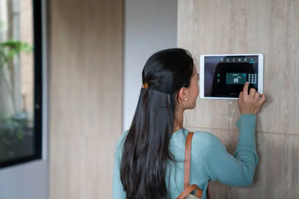Latin American woman entering pin to lock the door of her house using a home automation system - smart homes concepts. **DESIGN ON SCREEN WAS MADE FROM SCRATCH BY US**