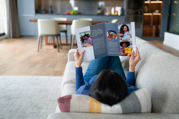 woman relaxing at home reading a magazine - magazine stockfoto's en -beelden