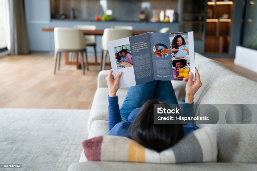 Woman relaxing at home reading a magazine Woman relaxing at home reading a magazine while lying down on the sofa - lifestyle concepts 
**DESIGN ON MAGAZINE WAS MADE FROM SCRATCH BY US** Magazine - Publication Stock Photo