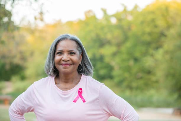 Senior woman with pink breast cancer ribbon on her shirt smiles while looking at the camera stock photo