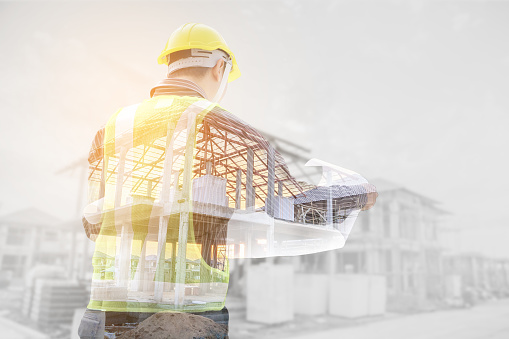 Double exposure image of professional engineer in protective helmet and blueprints paper at the house building construction site