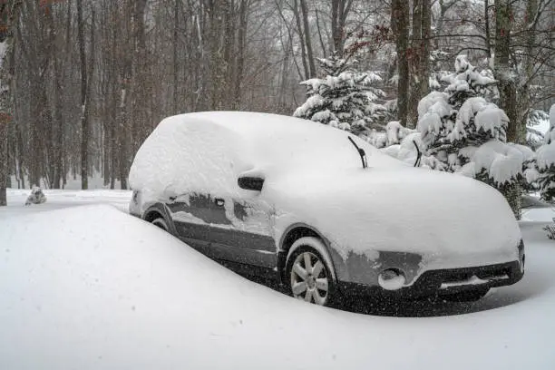 Photo of A car parked in the forest, trapped being covered with the show during a heavy winter snowstorm.