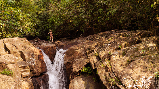 Tropical vacations in Sri Lanka. Mature Caucasian White woman walking on rocks around a small waterfall.