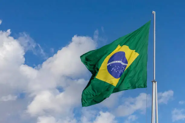brazil flag fluttering in the blue sky with clouds. Translation: order and progress.