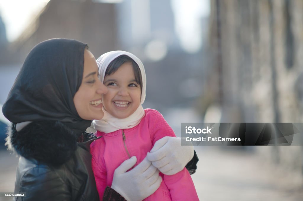 Muslim mother hugging her daughter A beautiful Muslim mother wearing a hijab is giving her young daughter a hug. They are standing on a street outside on a winter day. She is smiling ear to ear at her daughter. Afghan Ethnicity Stock Photo