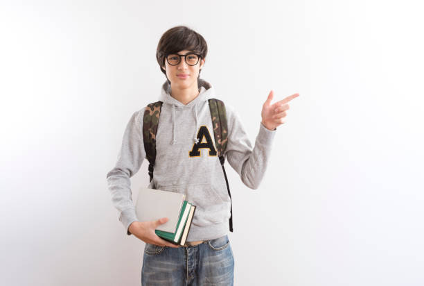 istock Handsome teen boy students carrying a backpack pointing finger standing on white background. 1337548612