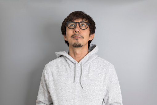 Adult asian man in grey sweater and glasses smiling on a grey background.