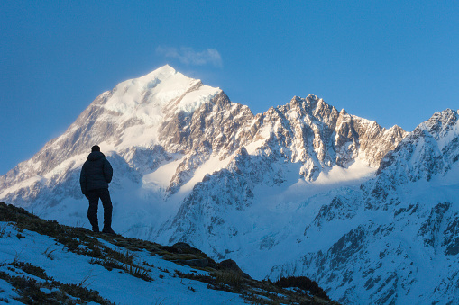 A hiker standing on hillside in Hooker Valley, below south faces of Aoraki Mount Cook and Nazomi