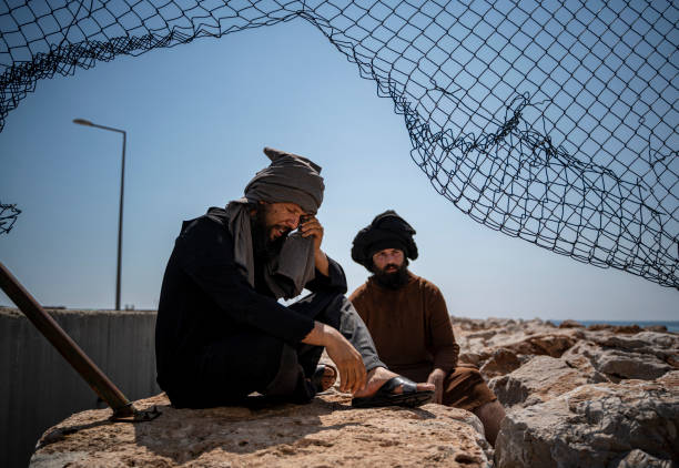 istock Two male refugee men sitting under the fence 1337559069