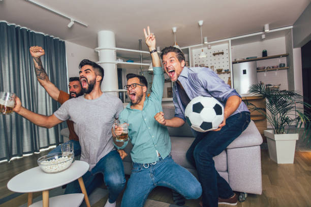 幸せな男友達やサッカーファンは、テレビでサッカーを見て、自宅で勝利を祝います。 - fan television football watching tv ストックフォトと画像