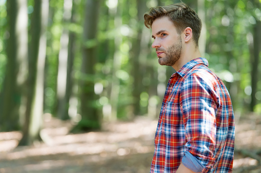 Handsome man travel in summer wood natural landscape sunny outdoors wearing plaid shirt in casual style, fashion.