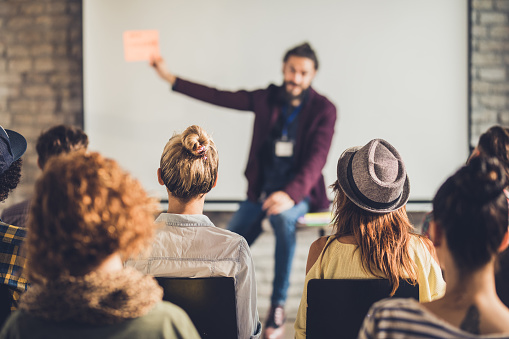 Back view of large group of people attending a seminar in a board room.