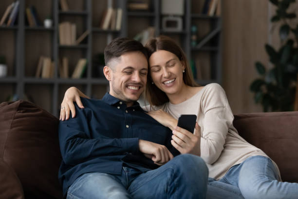 istock Happy couple sit on sofa use smartphone enjoy new application 1337568873