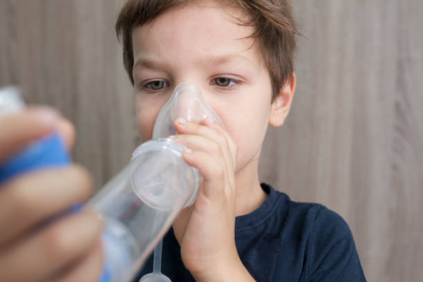 kinderjunge mit medizinischem spray für den atem. inhalator, abstandhalter und maske. seitenansicht - asthmatic child asthma inhaler inhaling stock-fotos und bilder